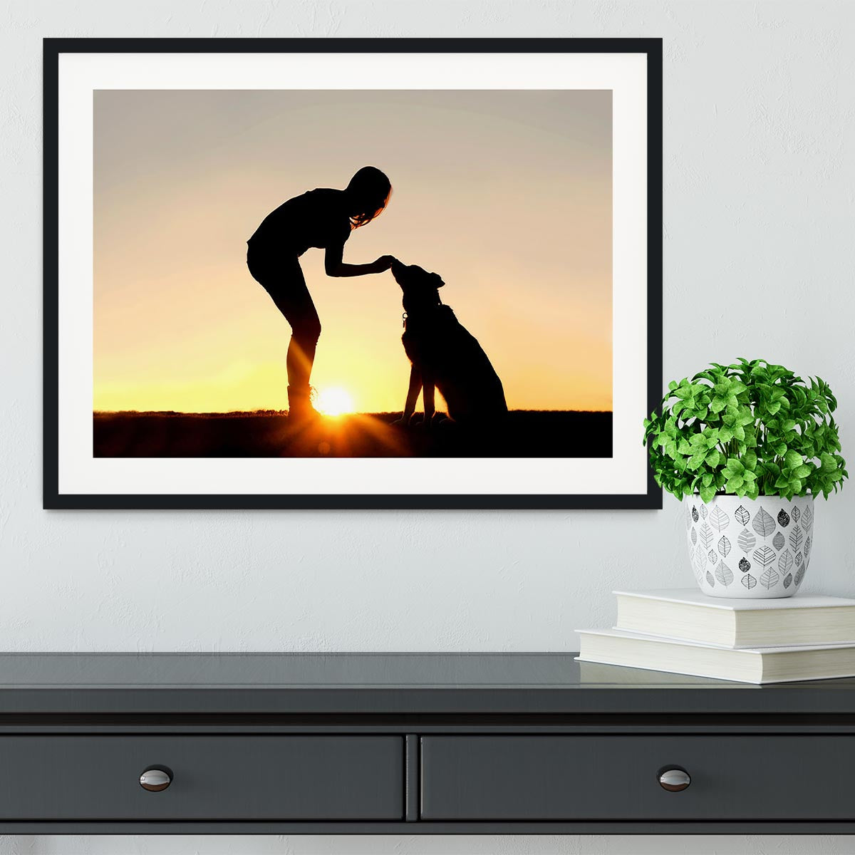 A silhouette of a girl sitting outside in the grass with her pet German Shepherd Mix Dog feeding him treats during training in front of a sunsetting sky. Framed Print - Canvas Art Rocks - 1